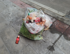Coca-Cola bottle next to a trash bag on a sidewalk